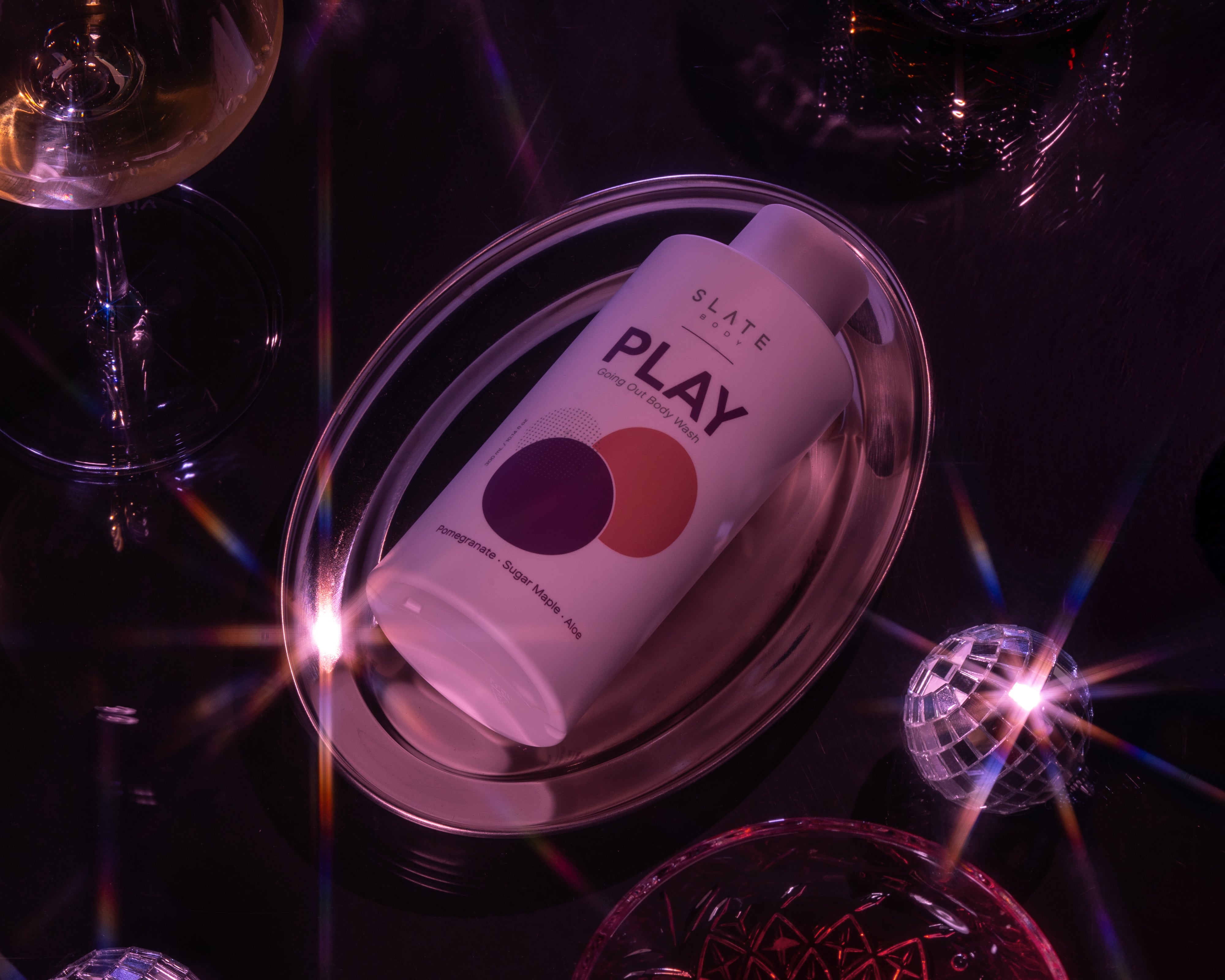Product packaging labeled 'PLAY' on a reflective surface with disco ball and wine glass in the background