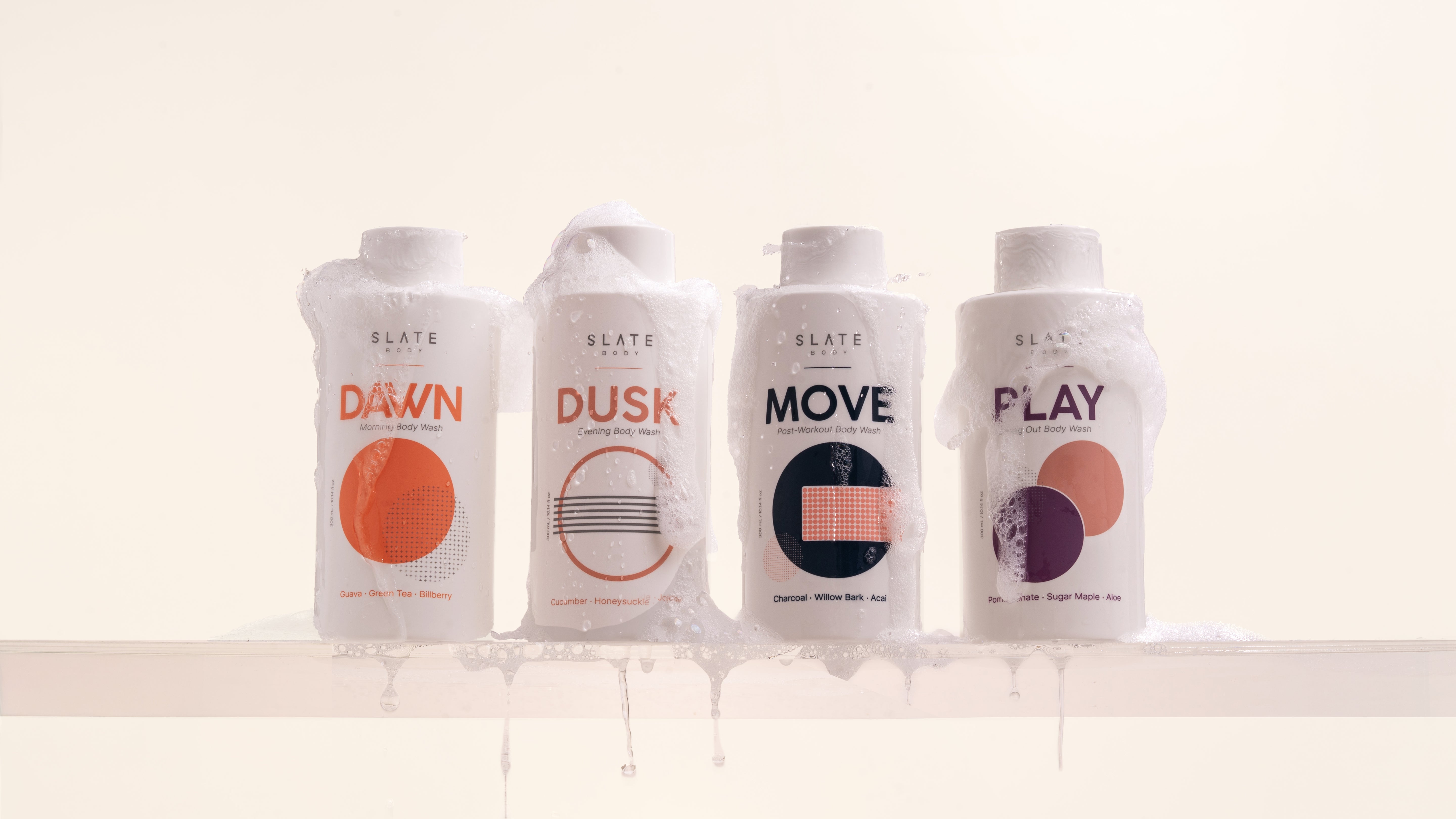 Four body wash product bottles labeled 'Dawn', 'Dusk', 'Move', and 'Play' on a white shelf.